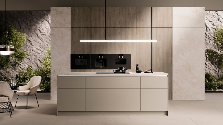 Moderne, minimalistische Küche mit zentraler Insel, Einbaugeräten an einer holzgetäfelten Wand und einer linearen Pendelleuchte; im Hintergrund ist die Grünanlage zu sehen.