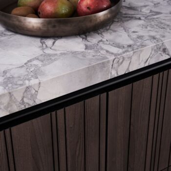 Eine Metallschale mit Obst steht auf einer grauen Marmorplatte von LEICHT, darunter ein holzgetäfelter KÜCHEN-Schrank.