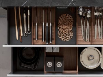 Leicht Küchen Contino E12 - Offene Küchenschublade mit Utensilien, Essstäbchen, Messern, Metalluntersetzern, Schüsseln, Tellern und schwarzen Behältern mit Deckeln unter einer Arbeitsplatte aus Marmor, die das elegante Design von Leicht Küchen unterstreicht.
