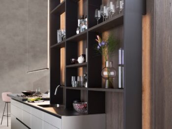 Leicht Küchen Contino E12 - Das moderne Design von Leicht Küchen bietet ein hohes, offenes Regal, in dem Gläser, Vasen und Dekorationsartikel ausgestellt werden können. Die elegante Arbeitsplatte Contino E12 enthält ein Spülbecken und sichtbare Kochzutaten für einen stilvollen, funktionalen Raum.