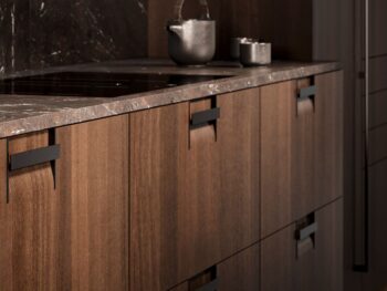 Leicht Küchen Griffkonzept Q - Modernes Leicht Küchen Design mit dunklen Holzschränken, eleganten schwarzen Griffen, einer grauen Steinarbeitsplatte und einer Teekanne aus Metall mit kunstvoll auf der Oberfläche angeordneten Tassen.