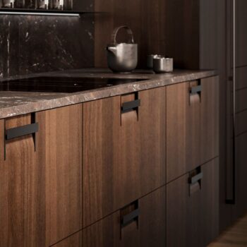 Leicht Küchen Griffkonzept Q - Modernes Leicht Küchen Design mit dunklen Holzschränken, eleganten schwarzen Griffen, einer grauen Steinarbeitsplatte und einer Teekanne aus Metall mit kunstvoll auf der Oberfläche angeordneten Tassen.