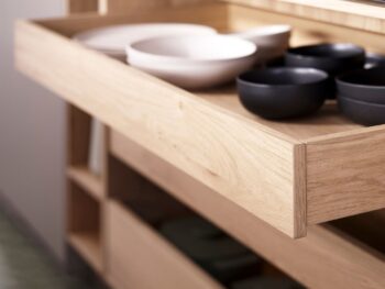Leicht Küchen KYOTO - Eine Nahaufnahme einer geöffneten Holzschublade von Leicht Küchen, in der weiße und schwarze Schalen übersichtlich angeordnet sind. Im Hintergrund ist ein Regal zu sehen - ein Hauch von KYOTO-Eleganz im modernen Küchendesign.