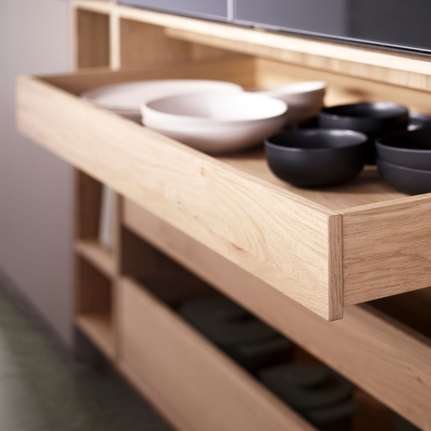 Eine Nahaufnahme einer geöffneten Holzschublade von Leicht Küchen, in der weiße und schwarze Schalen übersichtlich angeordnet sind. Im Hintergrund ist ein Regal zu sehen - ein Hauch von KYOTO-Eleganz im modernen Küchendesign.