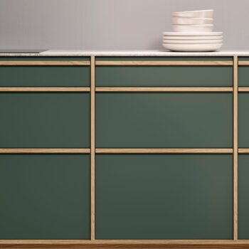 Leicht Küchen KYOTO - Ein Set aus dunkelgrünen Schränken von Leicht Küchen mit hellen Holzverkleidungen und einer weißen Arbeitsplatte, die mit gestapelten weißen Schalen und Tellern bestückt ist, zeugt von moderner Eleganz, inspiriert von KYOTO.