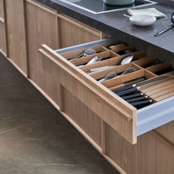Leicht Küchen KYOTO - In einer offenen Leicht Küchen-Schublade sind die Utensilien wie Messer, Gabeln, Löffel und KYOTO-Schneebesen in Holzfächern unter einer dunklen Arbeitsplatte übersichtlich angeordnet.