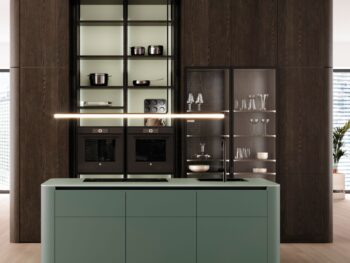 Leicht Küchen Rundwangen - Moderne Küche mit grüner Rundwangen-Insel, holzgetäfelter Wand, offenen Regalen mit Kochgeschirr und Gläsern sowie Einbaubacköfen von Leicht Küchen.