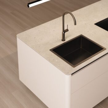 Leicht Küchen Rundwangen - Minimalistische Leicht Küchen-Insel mit einer Arbeitsplatte aus hellem Stein, einem quadratischen schwarzen Waschbecken und einer eleganten Armatur mit Rundwangen-Details auf einem hellen Holzfußboden.