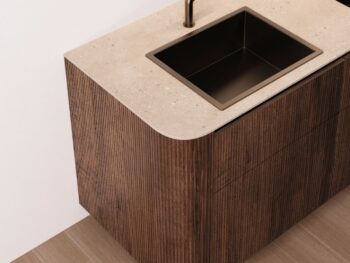 Leicht Küchen Rundwangen - Moderne Leicht Küchen Theke mit beiger Steinoberfläche, eingebautem rechteckigen Waschbecken, dunklem Wasserhahn, holzstrukturierten Schränken und eleganten Rundwangen-Details neben einem gefliesten Boden.