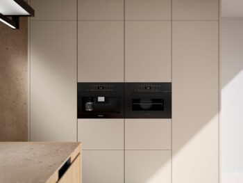 Leicht Küchen in der Trendfarbe Beige - Eine moderne Küche mit beigen Einbauschränken von Leicht Küchen, mit eingebauter Kaffeemaschine und Mikrowelle. Das natürliche Licht beleuchtet den Raum wie die Eleganz des Taj Mahal-Marmors.
