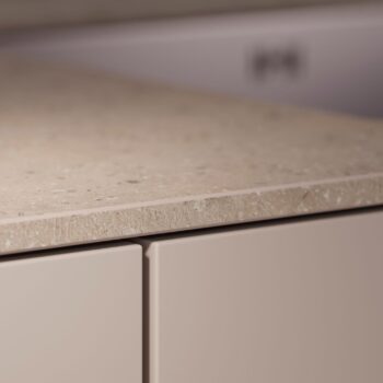 Leicht Küchen in der Trendfarbe Beige - Nahaufnahme einer beigefarbenen Arbeitsplatte mit Taj Mahal-Struktur und zwei glatten Schranktüren darunter, die die klaren Linien und die moderne Eleganz des Leicht Küchen Designs zeigen.