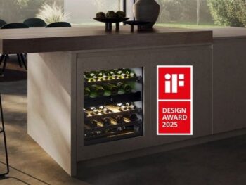 Ein eingebauter Weinkühler mit Flaschen im Inneren ist in eine Kücheninsel integriert; eine Plakette des iF Design Award 2025 ist am Schrank angebracht.