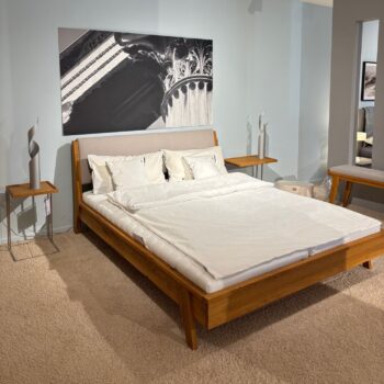 Ein modernes Retro-Massivholzbett mit weißer Bettwäsche steht zwischen zwei passenden Beistelltischen in einem mit Teppichboden ausgelegten Zimmer, mit einem schwarz-weißen Architekturfoto an der Wand über dem Kopfteil.