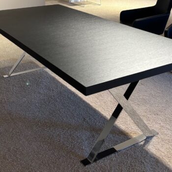 Ein moderner Maxalto-Schreibtisch mit dunkler, rechteckiger Platte und verchromten X-förmigen Beinen steht auf einem hellen Teppichboden und verbindet Stil und Funktion nahtlos - perfekt als eleganter Esstisch für zeitgenössische Räume.