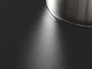 Nahaufnahme eines Edelstahltopfes auf einem Miele-Kochfeld, dessen glatte mattschwarze Oberfläche und der Topf das Licht elegant reflektieren.