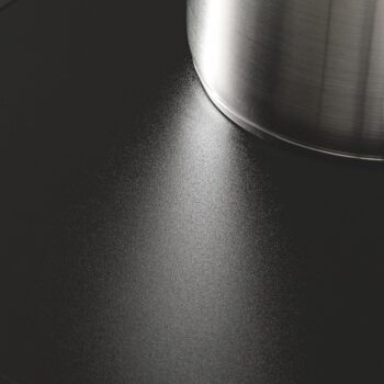 Nahaufnahme eines Edelstahltopfes auf einem Miele-Kochfeld, dessen glatte mattschwarze Oberfläche und der Topf das Licht elegant reflektieren.