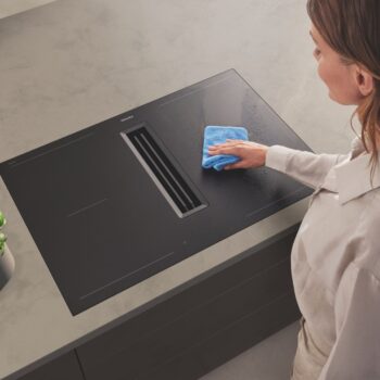 Mit einem blauen Tuch wischt eine Person die mattschwarze Oberfläche eines Miele-Induktionskochfeldes mit integrierter Dunstabzugshaube.