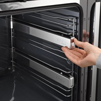 Eine Hand verstellt ein Metallgestell im Inneren eines modernen Miele-Backofens H 7464 BP mit schlichtem grauem Innenraum.