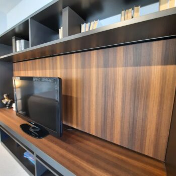 Ein Flachbildfernseher steht auf einem Holzregal der Molteni 505 Anbauwand vor einer gestreiften Holzverkleidung; auf den oberen Regalböden sind Bücher und eine kleine Figur ausgestellt.