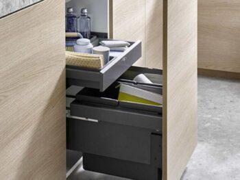 Ein Küchenschrank mit einem ausziehbaren Mülleimer und einer offenen Schublade für Reinigungsmittel, Schwämme und Flaschen.