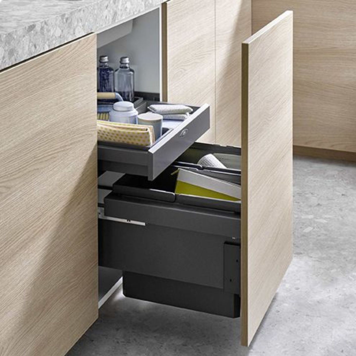 Ein Küchenschrank mit einem ausziehbaren Mülleimer und einer offenen Schublade für Reinigungsmittel, Schwämme und Flaschen. Ein Küchenschrank mit einem ausziehbaren Mülleimer und einer offenen Schublade für Reinigungsmittel, Schwämme und Flaschen.