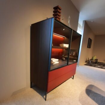 Ein modernes Molteni&C 505 UP Highboard verfügt über einen dunklen Holzrahmen, rote untere Schubladen und Glastüren, hinter denen ordentlich gestapelte Gegenstände zur Schau gestellt werden, und das alles in einem minimalistischen Raum.