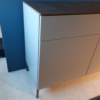 Ein modernes Sideboard von Molteni&C mit einer dunklen Holzplatte und hellen Türen und Schubladen, das auf Metallbeinen auf einem Teppichboden vor einer blauen Wand steht.