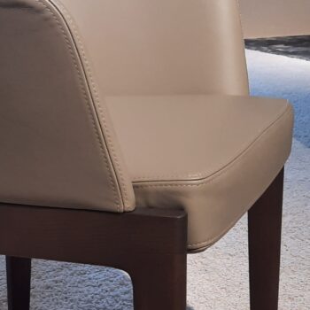 Nahaufnahme eines beige gepolsterten Chelsea Stühle von Molteni&C mit Holzbeinen auf einem hellen Teppich.