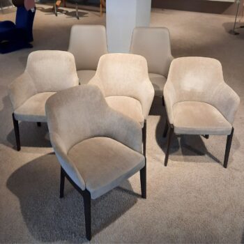 Fünf Molteni&C Chelsea Stühle mit beiger Polsterung und dunklen Beinen stehen auf einem Teppichboden, drei in der hinteren und zwei in der vorderen Reihe, und bilden ein elegantes Stühle-Set.