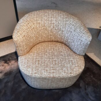 Der Molteni&C Elain Drehsessel, ein gepolsterter, runder Sessel aus strukturiertem beigem Stoff, steht anmutig auf einem dunklen Teppich auf einem hellen Boden.