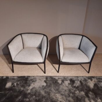 Zwei moderne Margou-Sessel von Molteni&C mit hellgrauer Polsterung und schwarzem Rahmen stehen nebeneinander auf einem Teppichboden vor einer schlichten Wand.