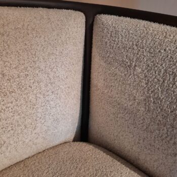 Nahaufnahme der Ecke eines beige gepolsterten Margou-Stuhls von Molteni&C, der seinen strukturierten Stoff und den dunklen Holzrahmen zur Geltung bringt.