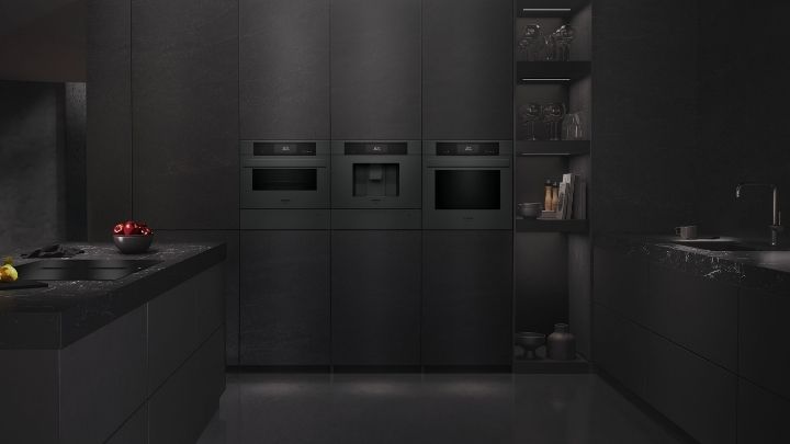 Siemens: Eine moderne Küche mit dunklen Schränken, Einbaugeräten, einer Arbeitsinsel mit Obst, offenen Regalen mit Küchenutensilien und einem Waschbecken auf der rechten Seite.
