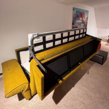 Ein gelbes „Dauerschläfer“-Sofa von Signet, das teilweise ausgeklappt ist und so seinen stabilen Metallrahmen sowie die bequeme Matratze im Inneren offenbart, steht auf einem beigen Teppich in der Nähe einer Wand, die mit einem farbenfrohen Stadtbild geschmückt ist – perfekt für den täglichen Gebrauch und stilvolle Entspannung.