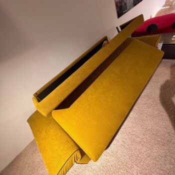 Ein senfgelbes „Dauerschläfer“-Sofa von Signet, dessen Kissen und Gestell voneinander getrennt sind, liegt ungeordnet auf einem beigen Teppichboden.