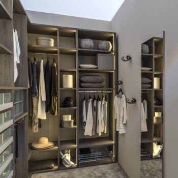 Ein begehbarer Kleiderschrank von Sudbrock mit offenen Regalen, hängender Kleidung, Aufbewahrungsboxen und einem Ganzkörperspiegel als zentrales Fokus-Element.