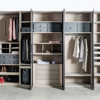 Ein großes, mehrteiliges Sudbrock-Kleiderschranksystem aus Holz mit Kleiderstangen, Schubladen, Einlegeböden und Aufbewahrungsboxen, die mit gefalteter Kleidung und Schuhen gefüllt sind.