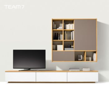 Modernes Wohnzimmer mit einer Team 7 Cubus Wohnwand, mit einem Flachbildfernseher auf einem niedrigen Schrank in Weiß und Holz, sowie Büchern und Dekoration auf einem passenden Wandregal.