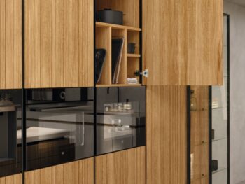 Ein moderner Team7-Küchenschrank mit vertikalen Holzpaneelen, die sich öffnen lassen, um Regale zur Aufbewahrung von Küchenutensilien und einen geschlossenen, in den Schrank eingebauten Backofen zu zeigen, präsentiert das elegante evo-Design und die zeitlose echt.zeit-Handwerkskunst.