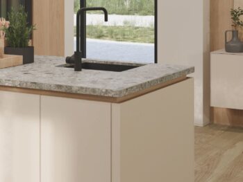 Eine moderne Küche mit einer Arbeitsplatte aus reinem Marmor, einem schwarzen Wasserhahn, beigen Schränken und einem großen Fenster, das den Blick auf einen grasbewachsenen Außenbereich freigibt - eine perfekte Verkörperung der eleganten Designphilosophie von Team7.