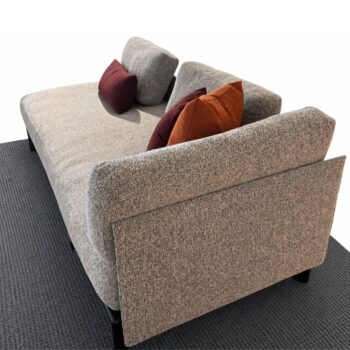 Ein modernes graues Vitra-Sofa, stilvoll gepolstert und mit zwei burgunderroten und einem braunen Zierkissen geschmückt – ein einladendes Synonym für Komfort –, steht auf einem dunklen, strukturierten Teppich vor einem makellos weißen Hintergrund.