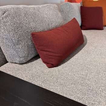 Graues, gepolstertes Vitra-Sofa mit strukturierten Kissen und zwei rechteckigen, weinroten Zierkissen, daneben eine schwarze Holzfläche.