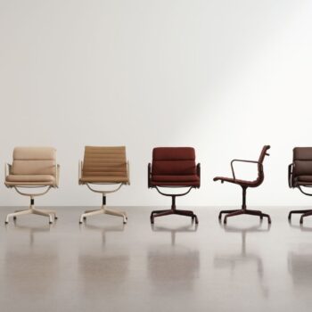 Fünf moderne Drehstühle, darunter der ikonische Vitra Soft Pad Chair EA 219, in neutralen und rötlich-braunen Tönen sind in einer Reihe vor einer schlichten weißen Wand auf einem polierten Boden angeordnet.
