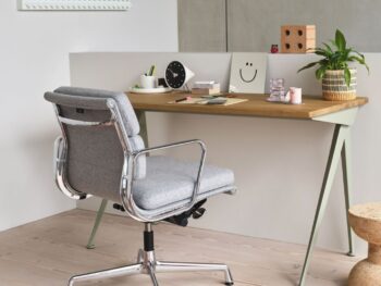 Ein moderner Arbeitsbereich mit einem Holzschreibtisch mit Schreibwaren, einer Pflanze, Dekorationsartikeln und einem Vitra Soft Pad Chair auf einem hellen Holzboden.