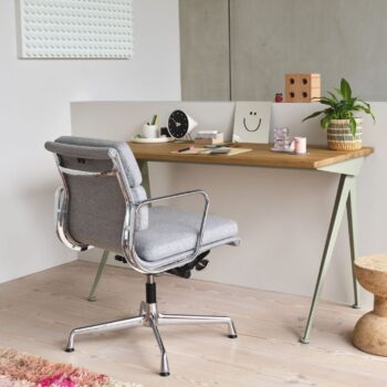 Ein moderner Arbeitsbereich mit einem Holzschreibtisch mit Schreibwaren, einer Pflanze, Dekorationsartikeln und einem Vitra Soft Pad Chair auf einem hellen Holzboden.