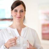 Frau in weißer Bluse, die ein Brustpumpenteil hält, steht in einem hellen, modernen Raum mit unscharfem Hintergrund. Frau in weißer Bluse, die ein Brustpumpenteil hält, steht in einem hellen, modernen Raum mit unscharfem Hintergrund.