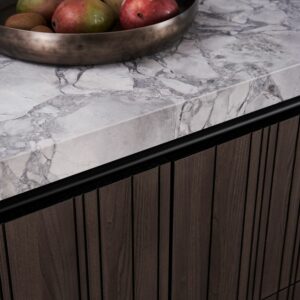 Die Nahaufnahme einer Marmorarbeitsplatte mit einer Obstschale über einem Holzschrank mit vertikaler Vertäfelung zeigt das raffinierte Design einer LEICHT Architekturküche.