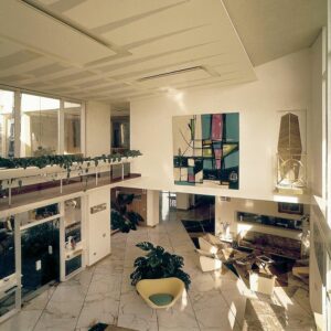 Modernes Wohnzimmer mit Marmorböden, großen Fenstern, zeitgenössischer Kunst, Zimmerpflanzen und minimalistischen Möbeln, darunter der ikonische Sessel D.154.2 von Gio Ponti, der um einen zentralen Couchtisch angeordnet ist.