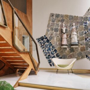Ein modernes Interieur mit einer Holztreppe, einem grünen gepolsterten Sessel D.154.2 und einer strukturierten Wandinstallation mit skulpturalen Figuren und Keramikfliesen.