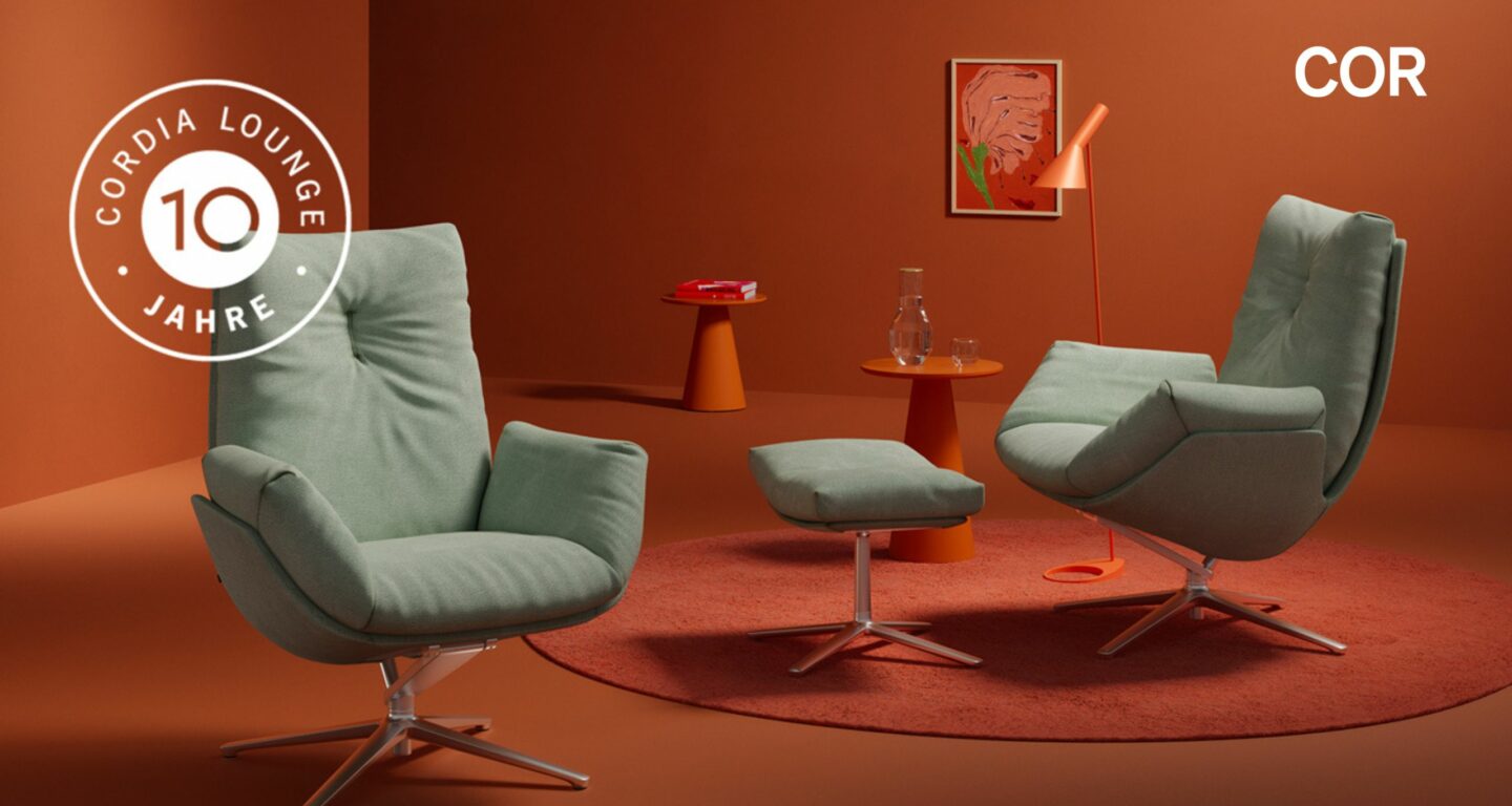 Zwei grüne Cordia Lounge Sessel mit passender Ottomane stehen auf einem orangefarbenen Teppich in einem modernen, orangefarbenen Raum und feiern Perfektion und Jubiläum mit 